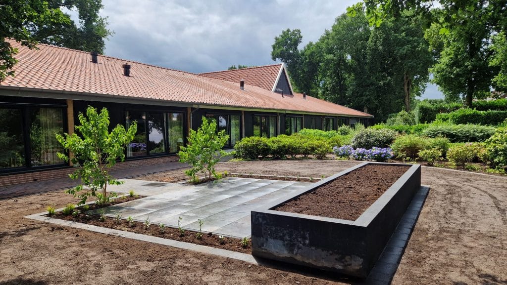 Verhoogde plantenborder met zwarte patioblokken en grijs terras met keramische tegels tijdens tuinrenovatie in Langeveen