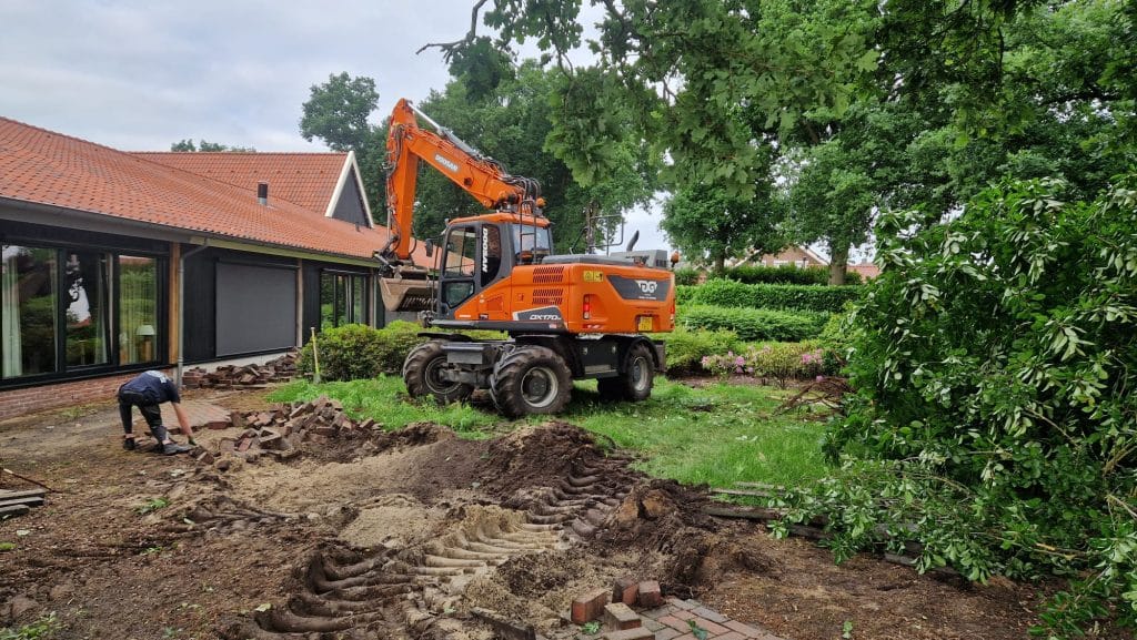 Graafmachine verwijdert oude klinkers tijdens start complete tuinrenovatie Erve Tijhuis Langeveen