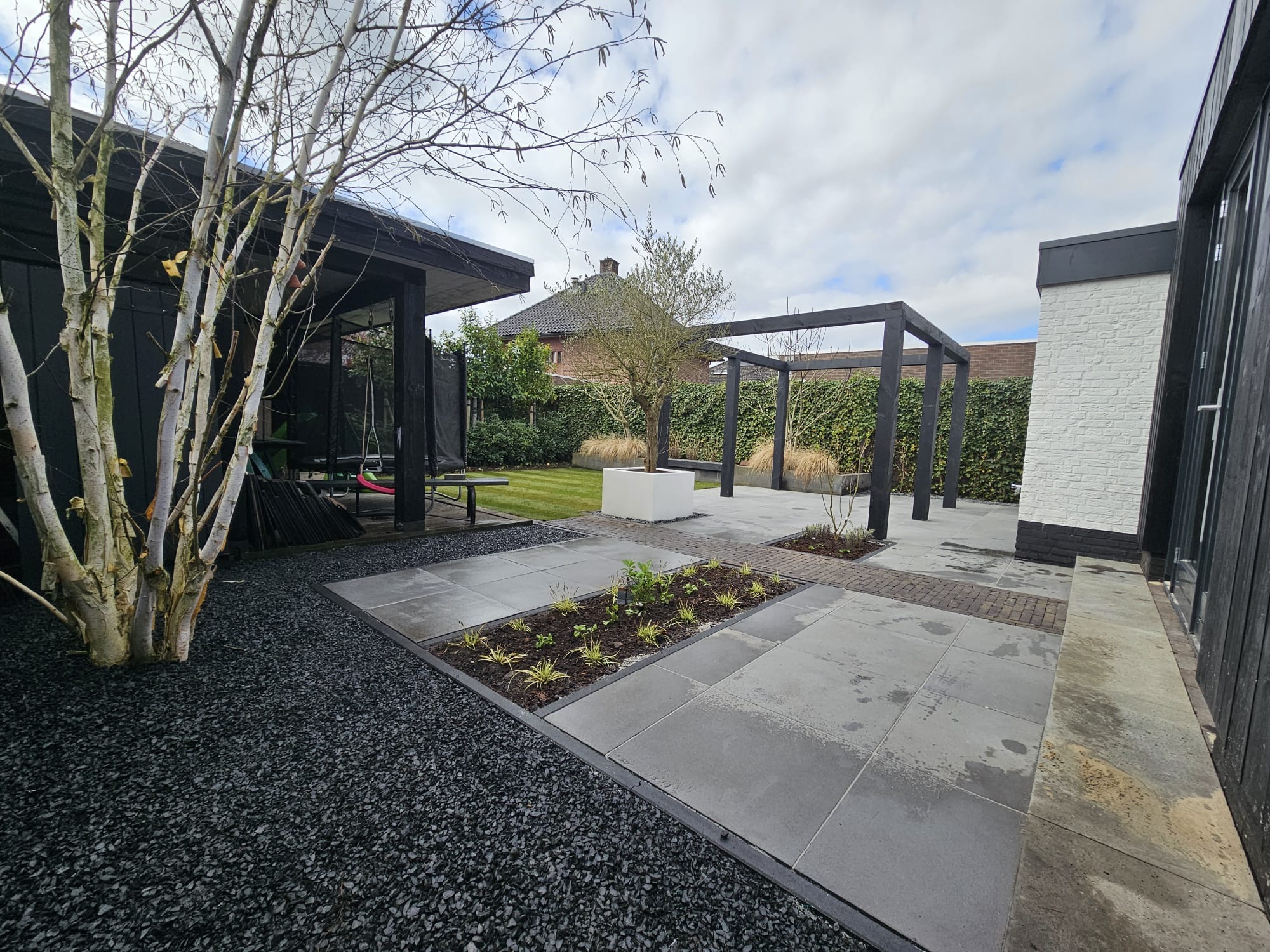 Achtertuin Albergen met zwarte pergola, witte plantenbak en strakke keramische tegels