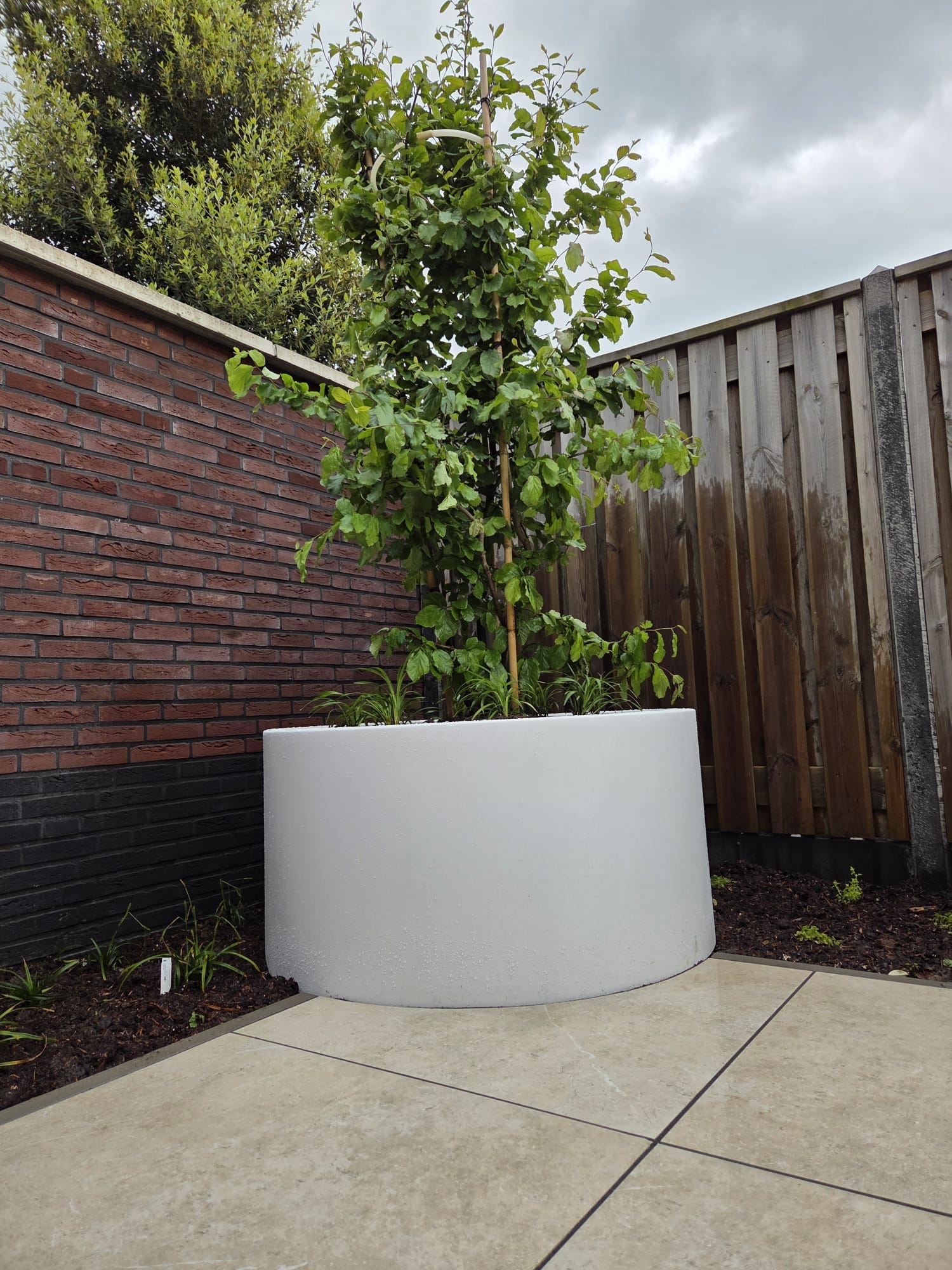 Witte ronde polyesterbak met boom in aangelegde achtertuin Tubbergen