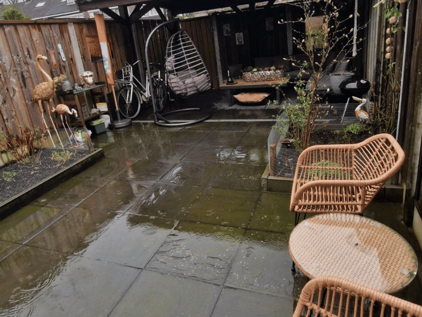 Oude achtertuin in De Lutte met grijze tegels en weinig groen voor de renovatie
