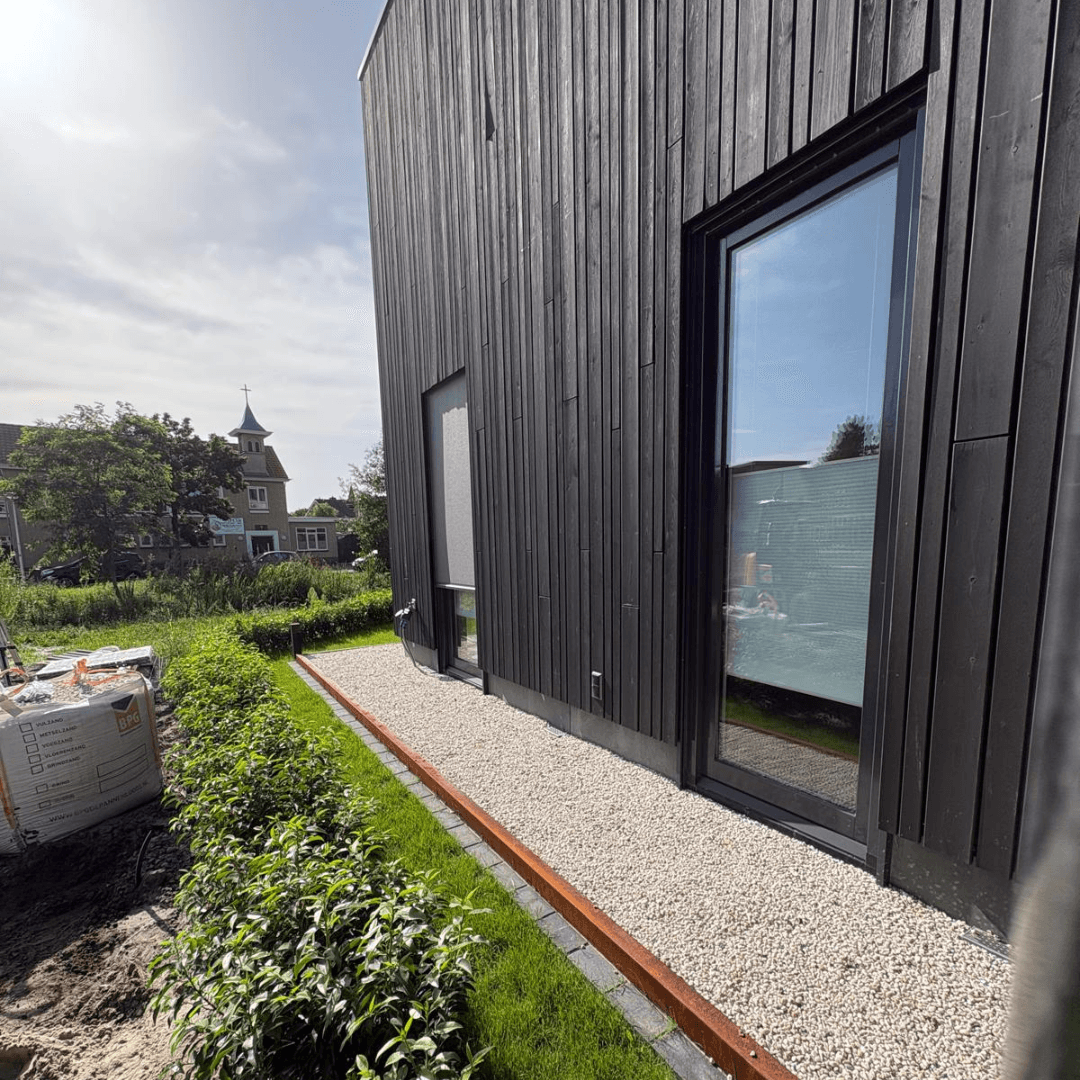 Grindstrook met cortenstaal rand langs de zwarte houten gevel van de nieuwbouwwoning in Hengelo