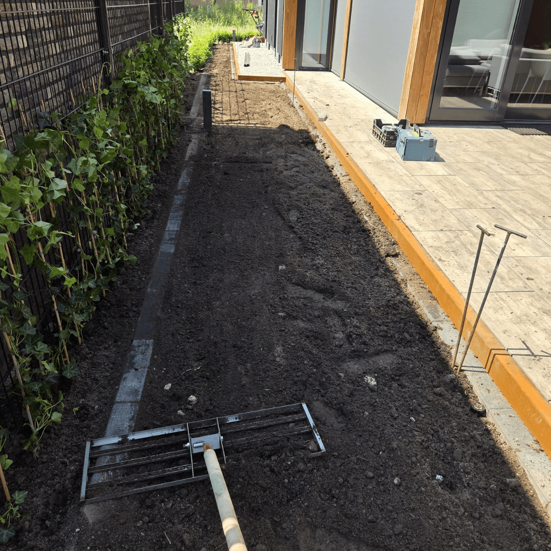 Grond egaliseren voor het gazon langs het hekwerk met hedera in de nieuwbouwtuin in Hengelo