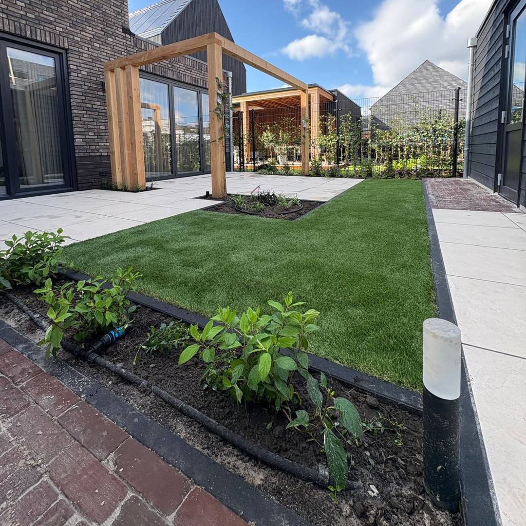 Jonge beplanting met beregeningsleiding naast kunstgras en klinkerpad in Hengelo